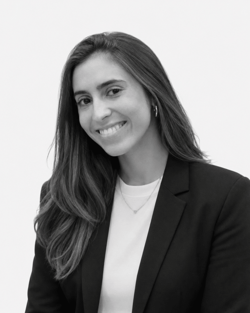 Smiling woman in a black blazer and white top posing for a professional headshot in black and white.