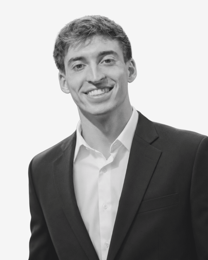 Professional headshot of a smiling man in a dark suit and white shirt against a light background.